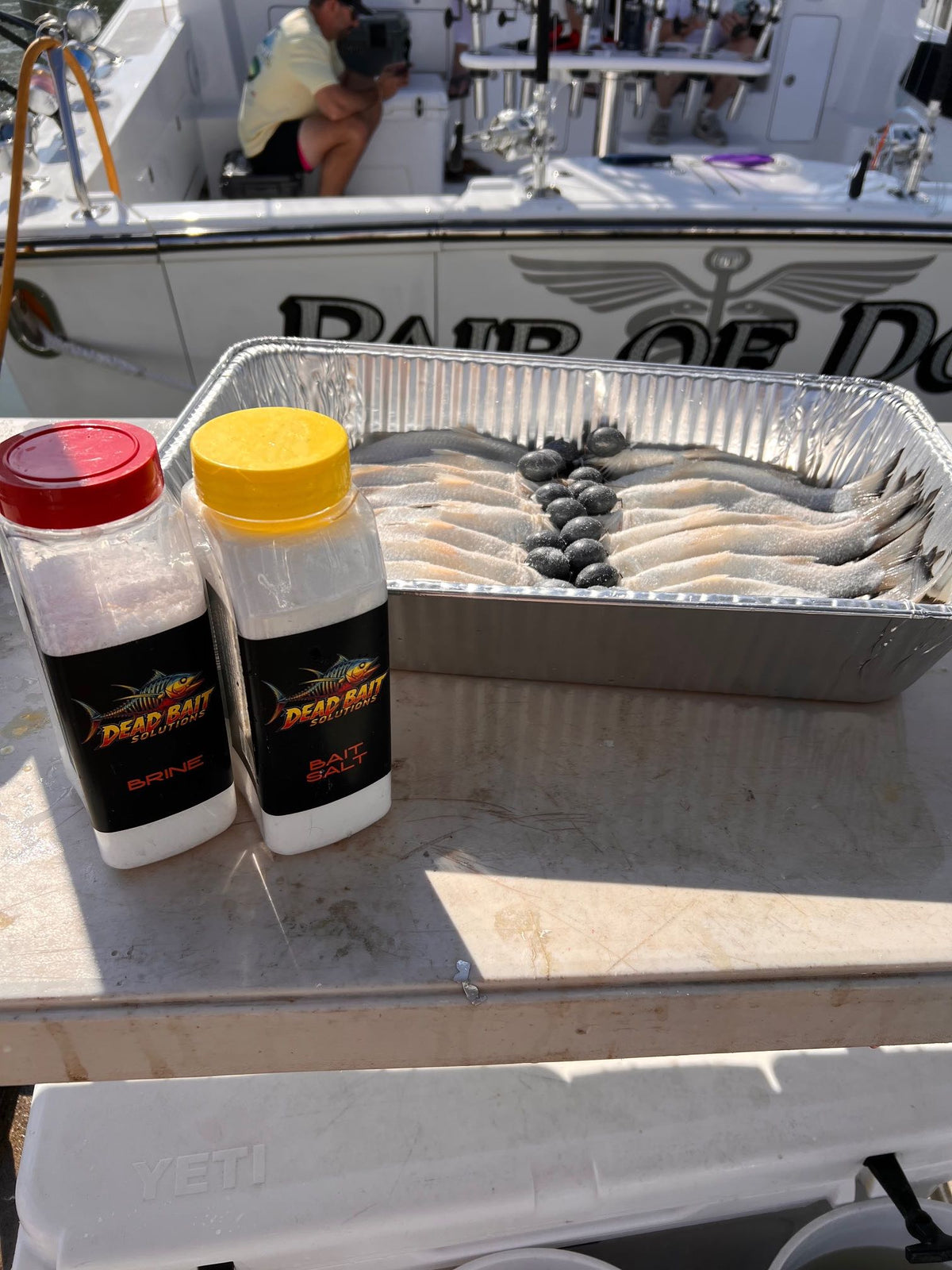 Two bottles of Dead Bait Salt on a boat with a tray of fish.